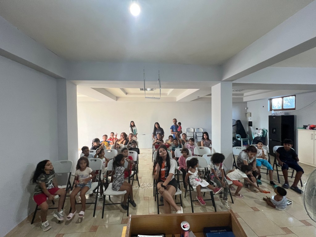 Two beach chairs under an umbrella on a sandy beach. The chairs have blue and white striped fabric and the umbrella has a ...
