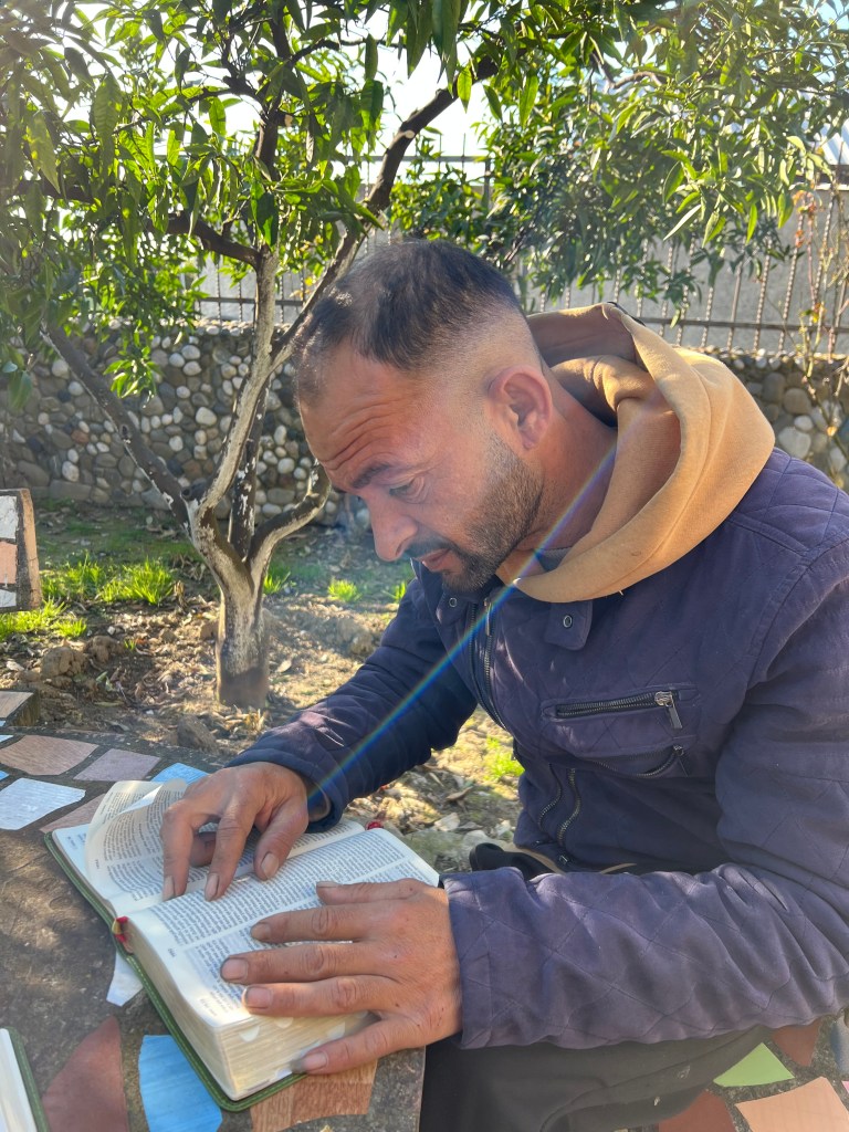 A stack of round chocolate chip cookies on a dark brown plate lined with parchment paper, surrounded by bowls of flour, br...